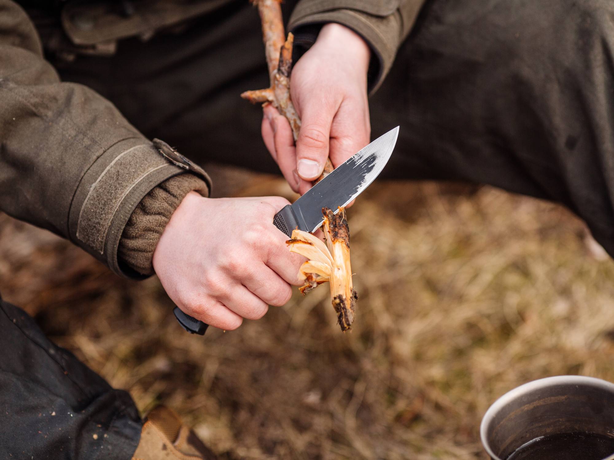 An outdoor adventurer using their carefully selected outdoor knife to whittle wood for a campfire.
