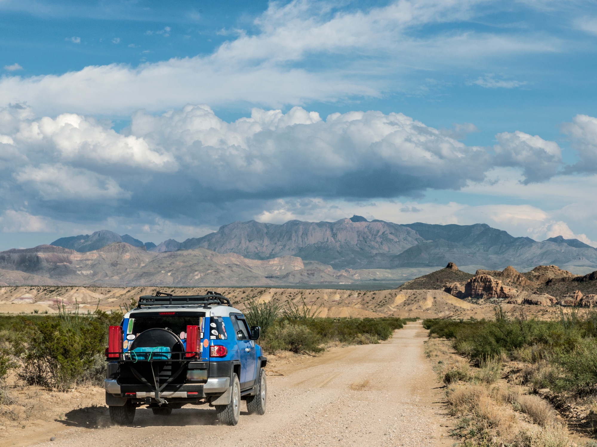 A blue 4x4 vehicle driving along a dirt path in Big Bend National Park in Texas. Mountains are visible in the distance.