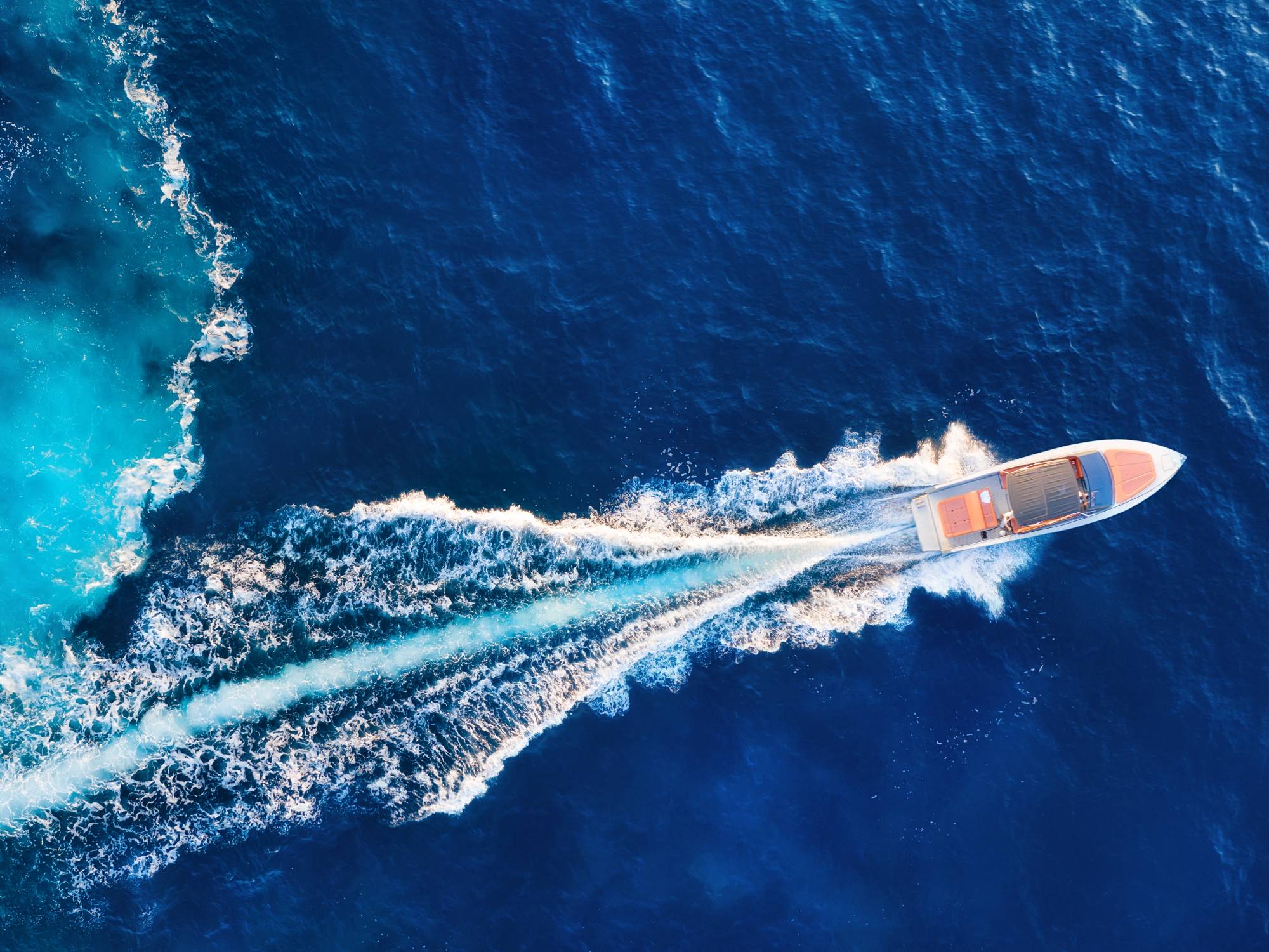 An overhead view of a speedboat moving across a body of bright blue water with a large wake left behind.