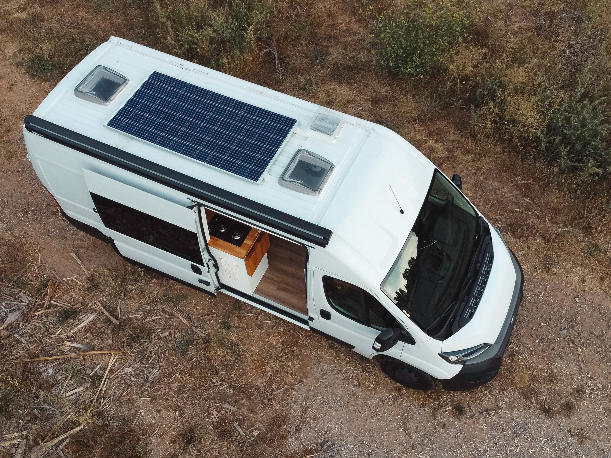 An overhead view of an RV camper with solar panels on its roof. The door is open and its inside is visible.